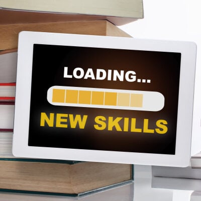 tablet screen reads "LOADING... NEW SKILLS" with a yellow progress bar; in the background are books