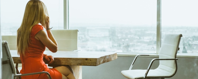 professional woman in orange sheath dress sitting at conference table;  talking on cell phone and looking at cityscape from skyscraper window