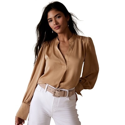 A woman wearing a brownish-gold blouse with white trousers and a beige belt