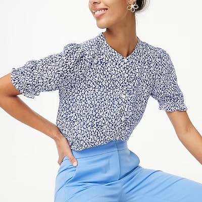 A woman wearing a blue-and-white print blouse and light-blue pants, with flower-shaped earrings