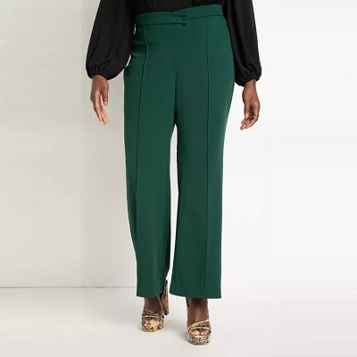 A woman wearing a black top with green tailored pants and snakeskin-print sandals
