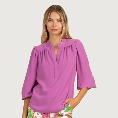 A woman wearing a V-neck dark lavender top and brightly colored pants with butterflies 