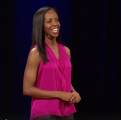 Sarah Lewis, a Black woman in a pink sleeveless top, gives a TED talk in front of a dark background