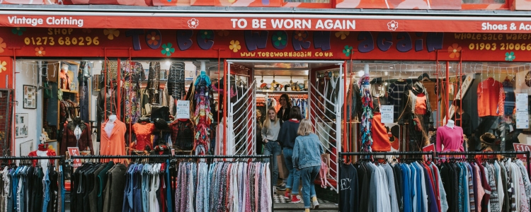 BRIGHTON, ENGLAND - October 24th, 2018: Vintage clothing shop facade with a lot of clothes in the street, and people entering inside it. 