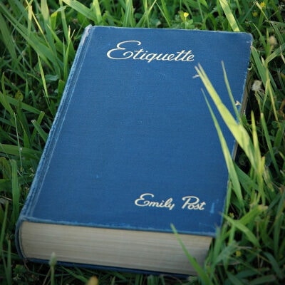 blue hardcover book sits in the grass; the title is "Etiquette," by Emily Post