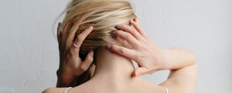 blonde woman in strappy camisole touches the back of her neck and head; she is wondering how to fix tech neck
