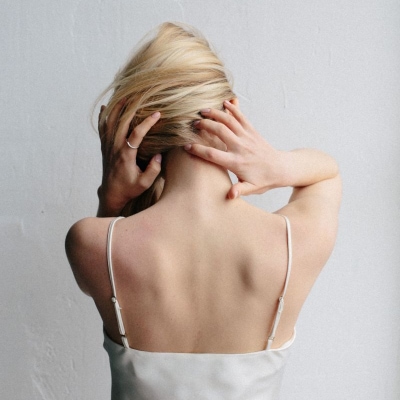 blonde woman in strappy camisole touches the back of her neck and head; she is wondering how to fix tech neck