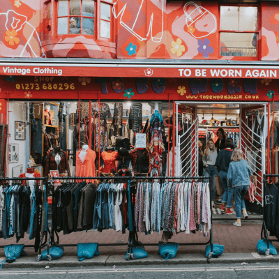 BRIGHTON, ENGLAND - October 24th, 2018: Vintage clothing shop facade with a lot of clothes in the street, and people entering inside it.