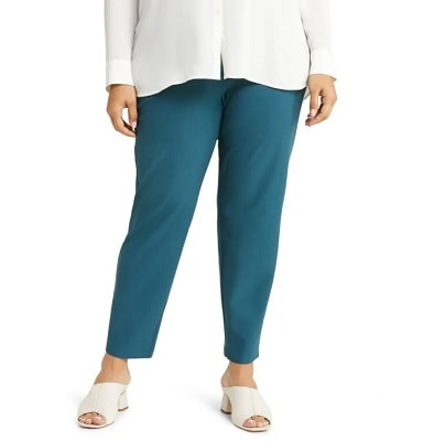 A woman wearing a white blouse, teal pants and white sandals