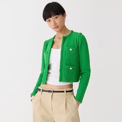 A woman wearing a green sweater-jacket, a white top, khakis, and a black belt