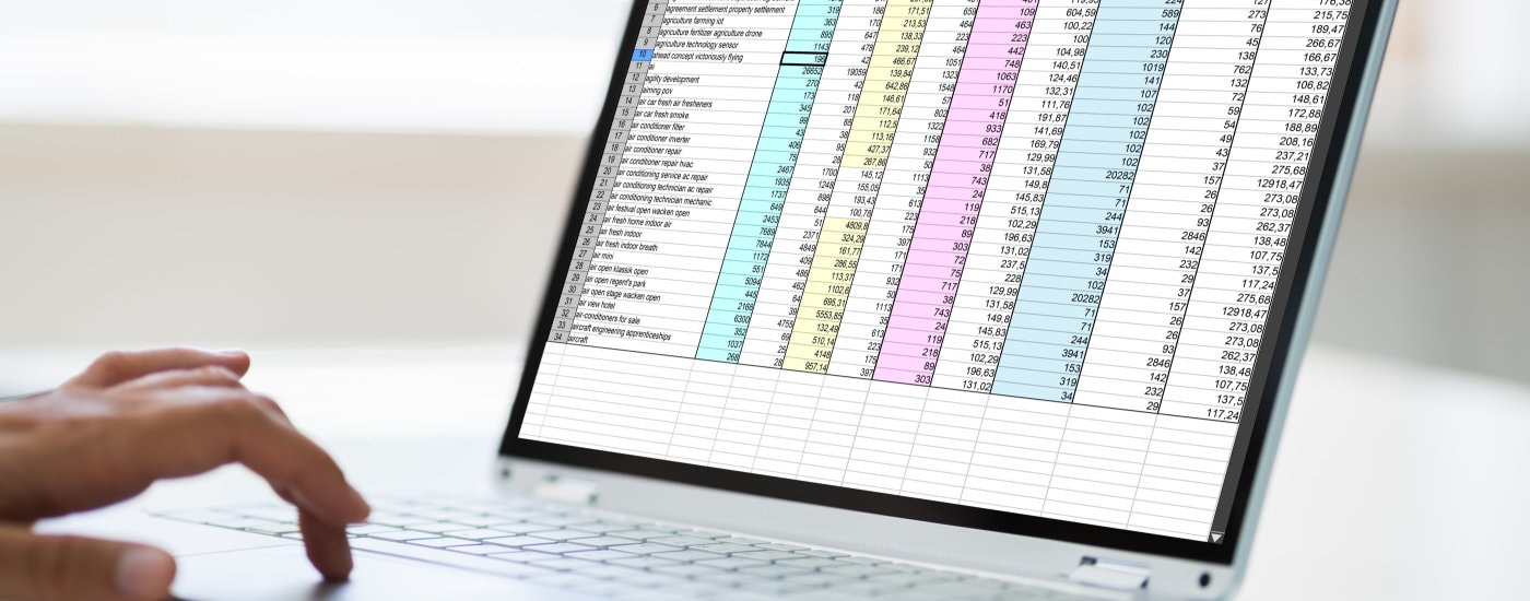 woman's hand hovers over keyboard while she studies an Excel spreadsheet