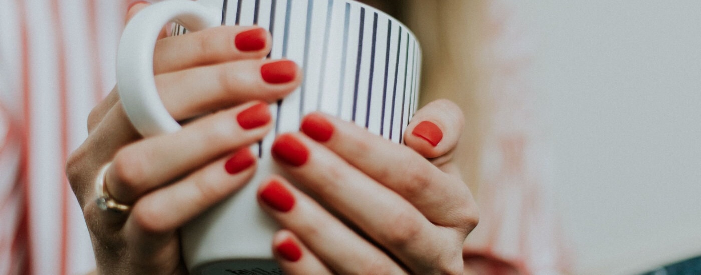 young professional woman holds coffee cup; she has short red nails