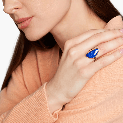 темно-синее массивное кольцо слегка треугольной формы;  модель носит светло-персиковый свитер и держит руку на плече, чтобы показать кольцо
