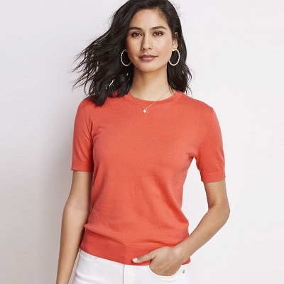 A woman wearing an orange short sleeve sweater and white pants