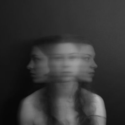 artsy overexposed photo to suggest woman has anxiety: the blurred image shows her looking directly at camera, as well as to both sides, all at once