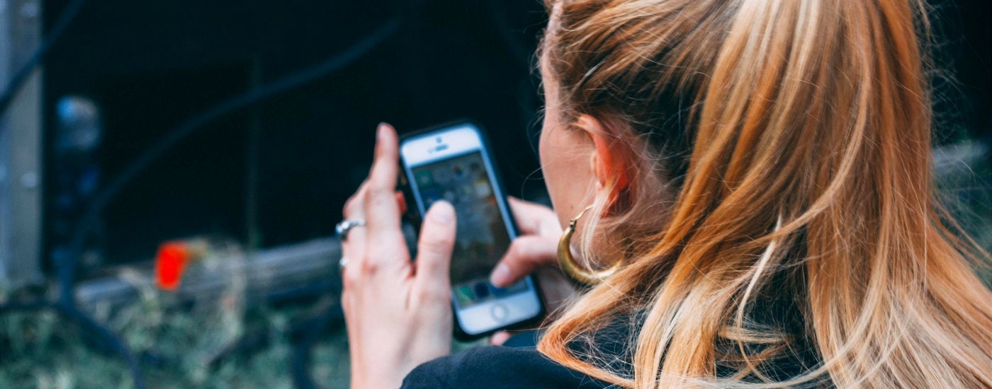 woman with reddish hair in a ponytail scrolls through her phone;  you're looking over your shoulder