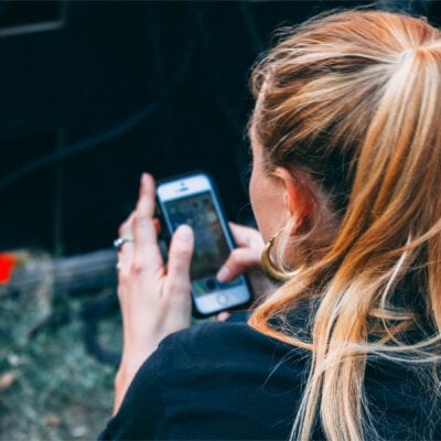 woman with reddish hair in pony tail scrolls through her phone; you are looking over her shoulder
