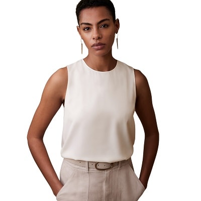 A woman wearing a white sleeveless top with off-white pants and a matching belt