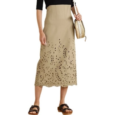 Woman wearing black blouse, nude midi skirt, black sandals and carrying a reed bag
