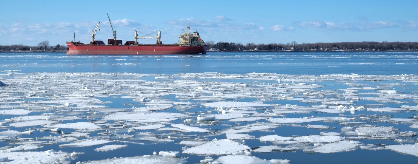 um barco quebra-gelo vermelho (no fundo ao longo do horizonte) em um corpo de água com gelo flutuante em primeiro plano