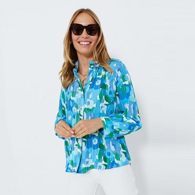 A woman wearing sunglasses, a blue patterned shirt and white pants