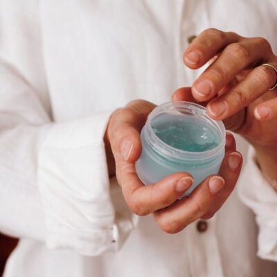 woman wearing white dips her finger into a jar of blue gel