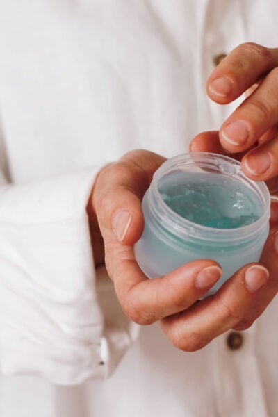 woman wearing white dips her finger into a jar of blue gel