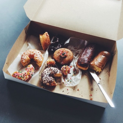 A cardboard box containing half-eaten doughnuts and pastries, with a white plastic knife