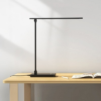 A black desk lamp on top of a wooden table next to a magazine