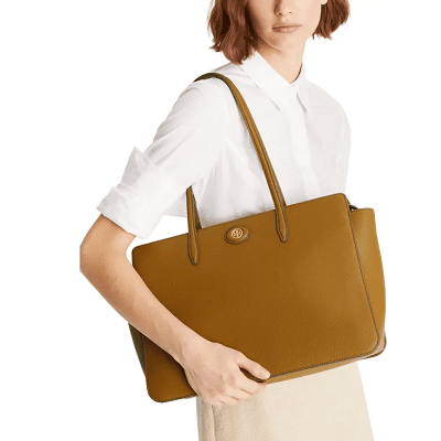 woman has tan leather tote over her arm; she wears a white blouse and a beige skirt
