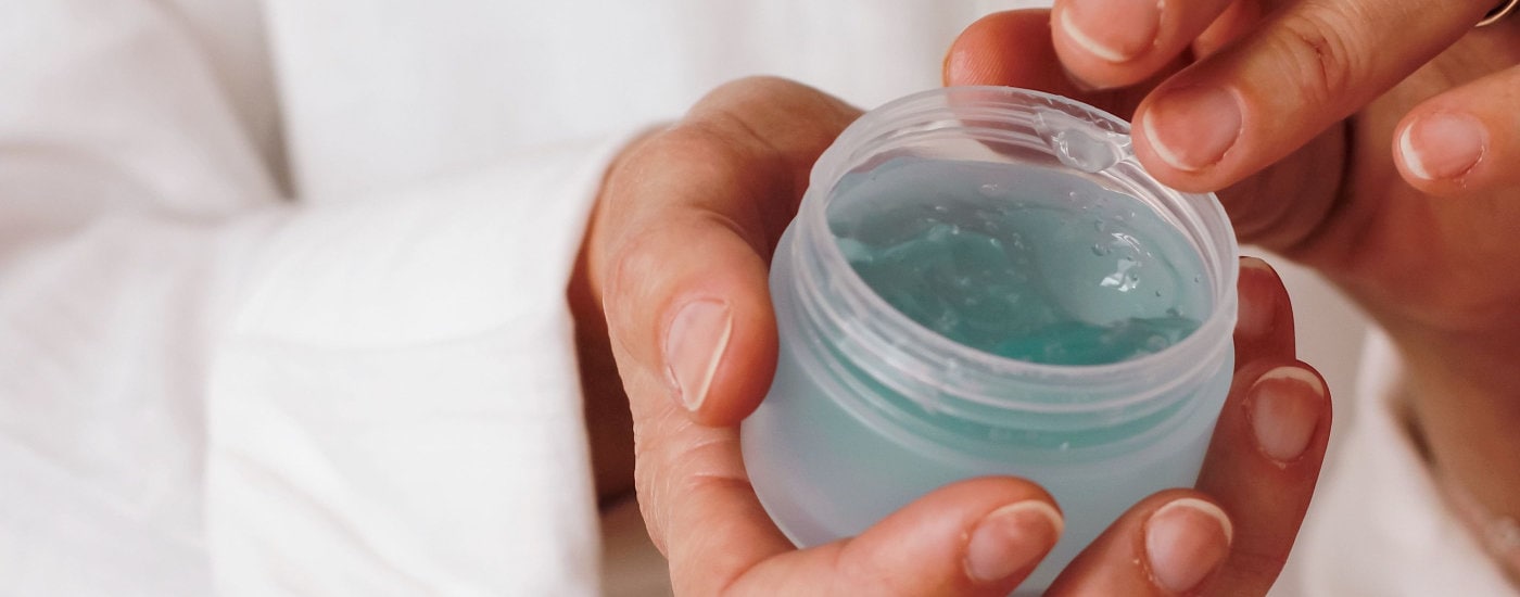 woman wearing white dips her finger into a jar of blue gel