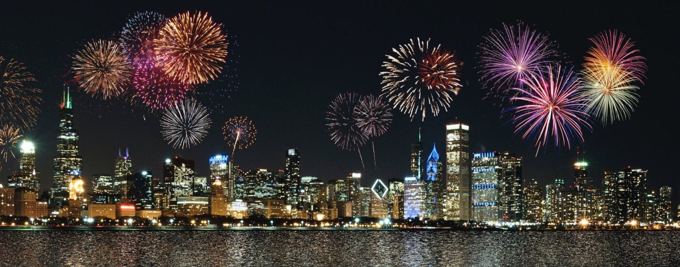 colorful fireworks explode above a city skyline at night; the view is across a body of water