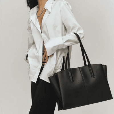 woman wearing barely-buttoned white button-front blouse carries a black vegan laptop tote