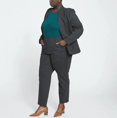 Black plus-size model wears stylish plus-size work pants, a teal sweater, and a blazer with nude-for-her heels