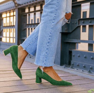 woman stands on boardwalk wearing ripped blue jeans and green suede heels