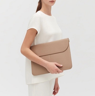 woman holds beige "tech carryall" envelope that can hold a laptop; she is wearing all ivory