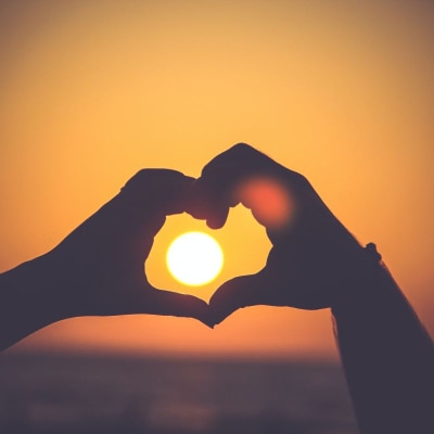 two hands circle the sun (on the horizon), forming a heart shape