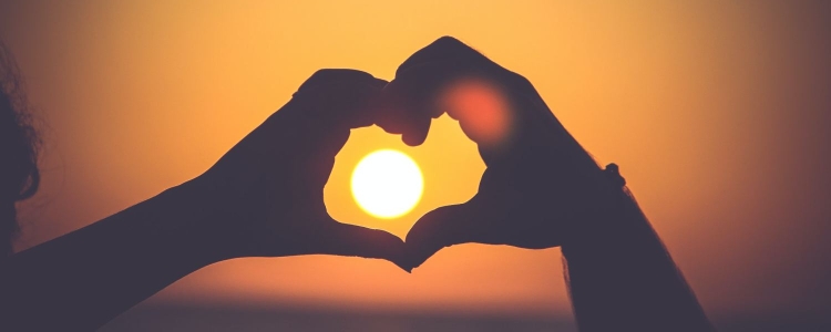 two hands circle the sun (on the horizon), forming a heart shape