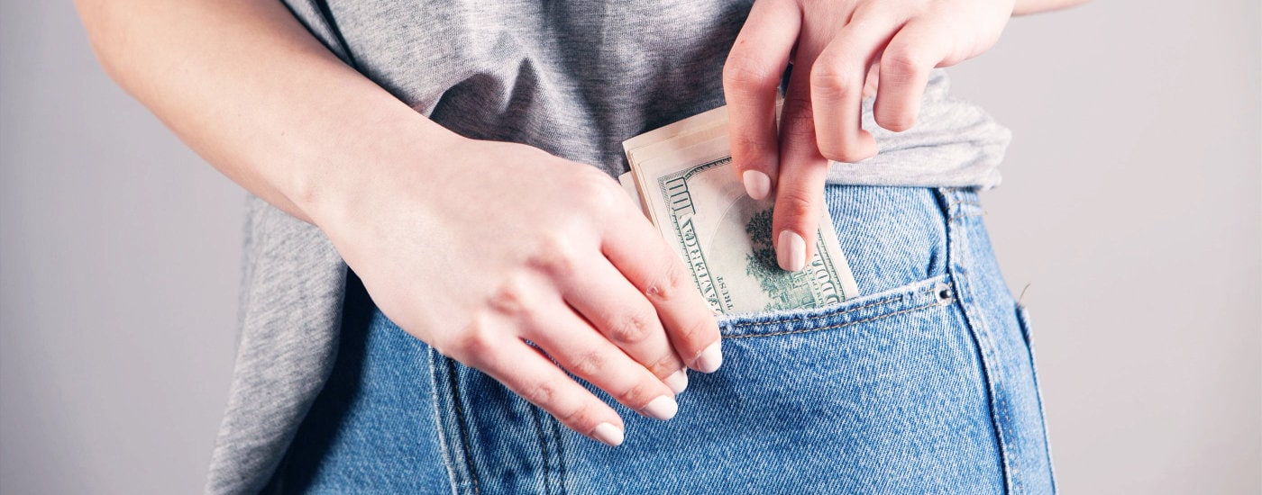 woman puts $100 bills into her pocket because she's saving more money