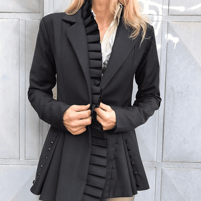 dramatic blazer with lots of pleats; woman stands against wall