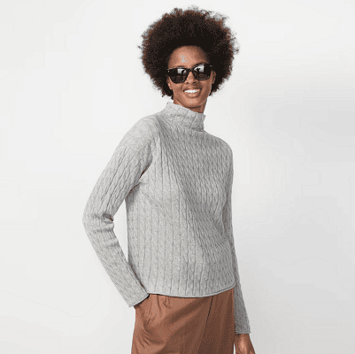 woman smiles while wearing a gray 100% cotton mock neck roll neck; she also wears a brownish skirt and black sunglasses