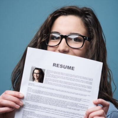 young professional woman hides behind her resume; she is wondering how often she should update her resume
