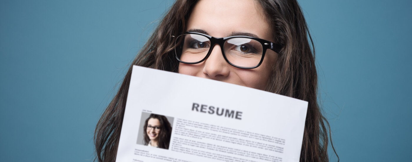 young professional woman hides behind her resume; she is wondering how often she should update her resume