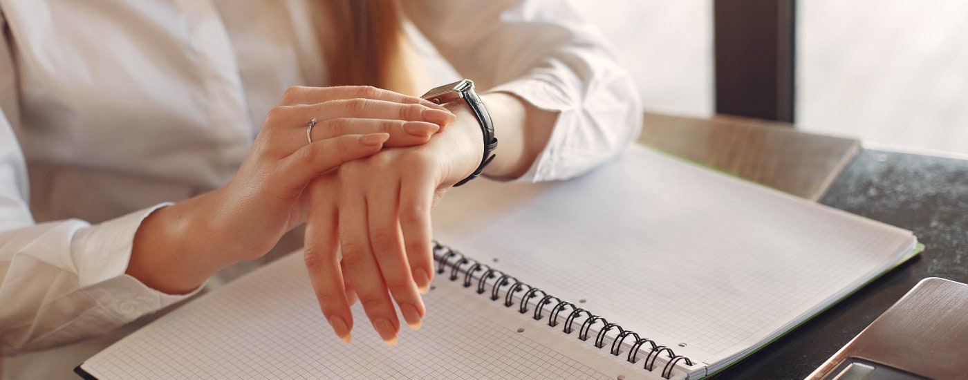 young professional woman looks at her watch; she has an open gridded notebook open in front of her