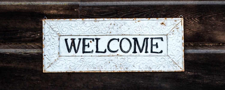 signs reads WELCOME; sign is metal with some rusting and scrollwork detail around the frame