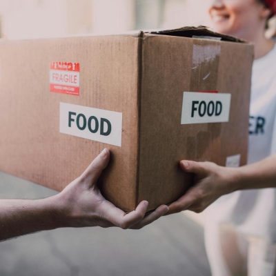 woman hands a cardboard box labeled FOOD to another person