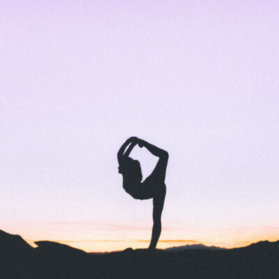 woman does yoga at sunset; she is holding an advanced yoga pose