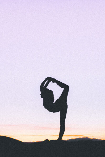 woman does yoga at sunset; she is holding an advanced yoga pose