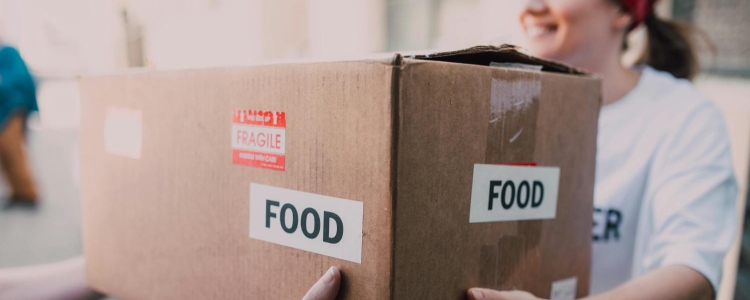 woman hands a cardboard box labeled FOOD to another person