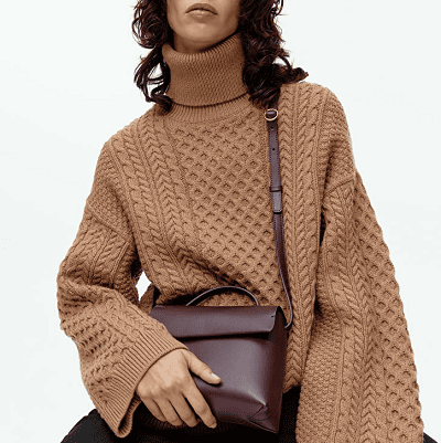 woman in light brown cableknit sweater holds a burgundy leather shoulder bag